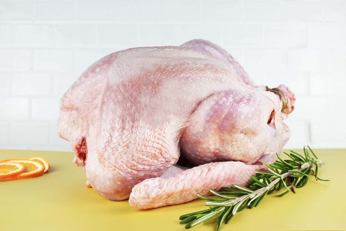 Rohe, ungewürzte kleine Pute liegt auf gelber Fläche neben Rosmarinzweig und Orangenscheiben.