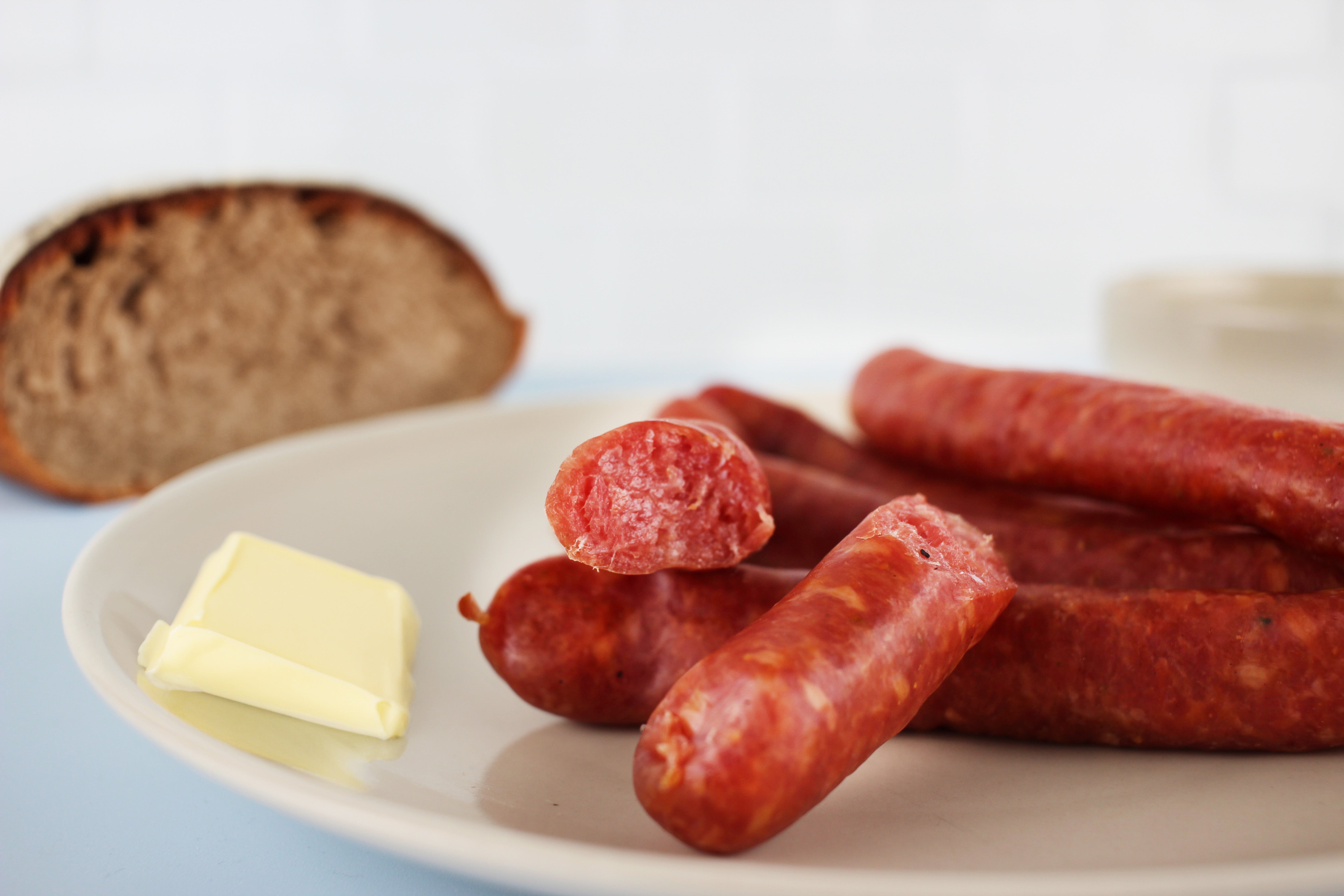 Mehrere rote Bierwürstchen auf einem weißen Teller, daneben ein Stück Butter und im Hintergrund eine Scheibe Brot