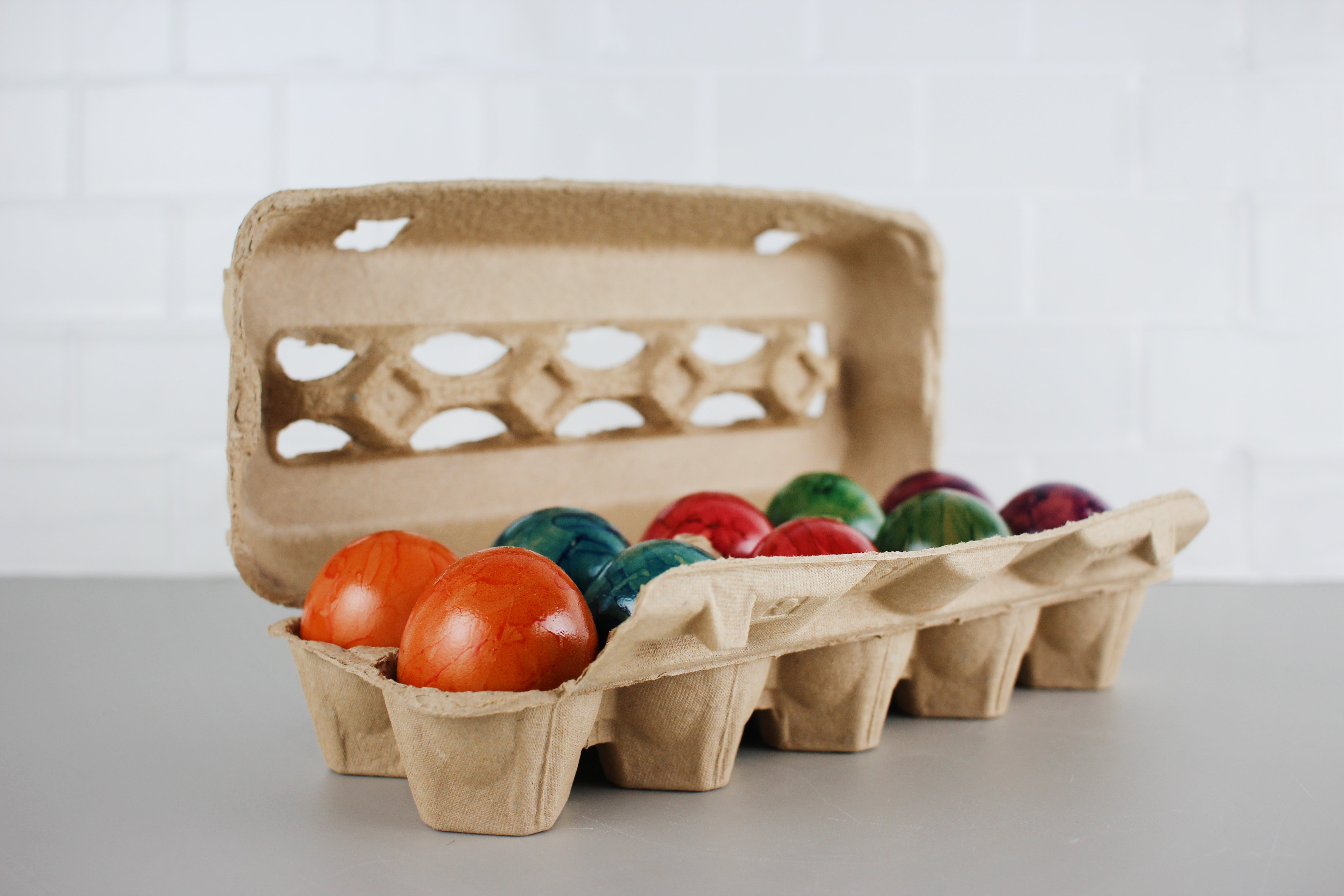 Bunte bemalte Hühnereier in einem Eierkarton mit orangefarbenen, grünen, roten und blauen Farbtönen auf hellem Hintergrund.