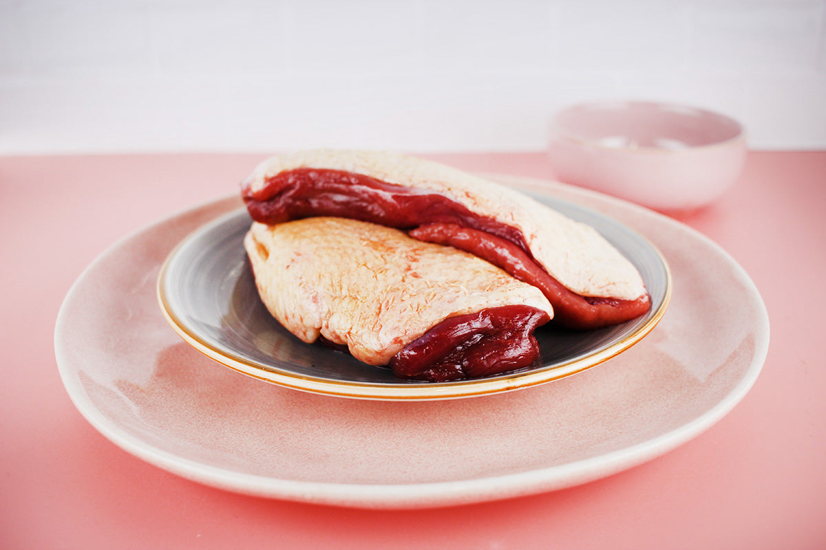 Zwei rohe Entenbrustfilets mit Haut auf einem grauen Teller, der auf einem größeren rosa Teller steht