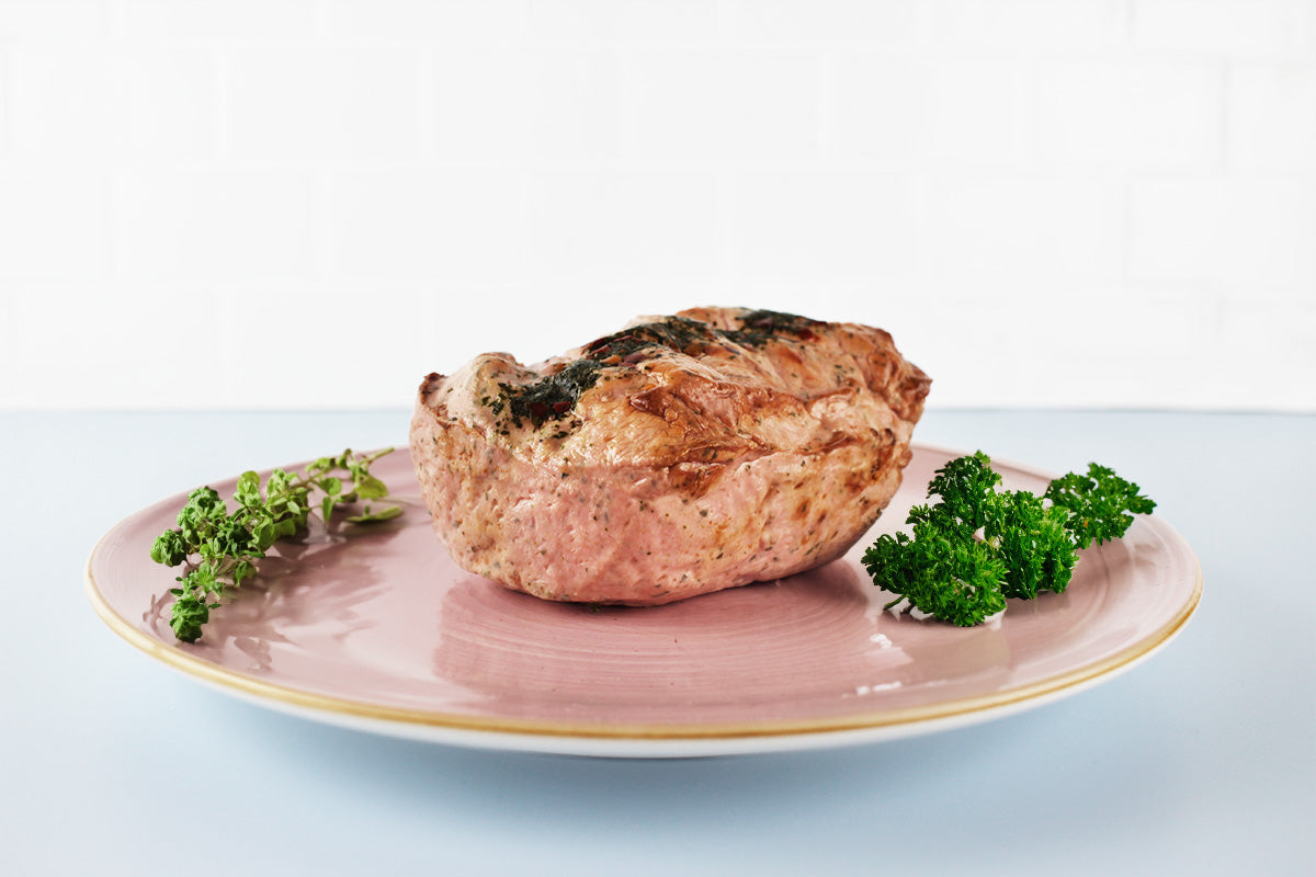 Gebratenes Fleischstück auf rosa Teller, garniert mit frischen grünen Kräutern.