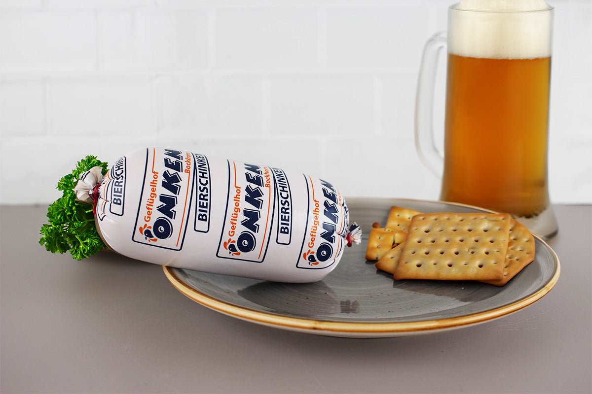 Geflügelbierschinken von Onken auf grauem Teller mit Crackern und volles Bierglas im Hintergrund