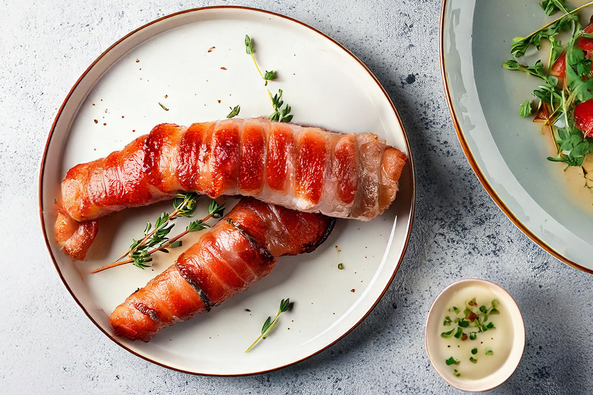 Gegrillter Kaninchenrücken im Speckmantel auf weißem Teller mit Thymianzweigen, daneben Wildkräutersalat und kleine Schale mit Sauce