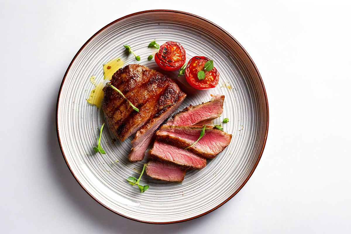 Gegrilltes Entenfilet, in Scheiben geschnitten, mit gegrillten Tomaten und grünen Kräutern auf einem weißen Teller