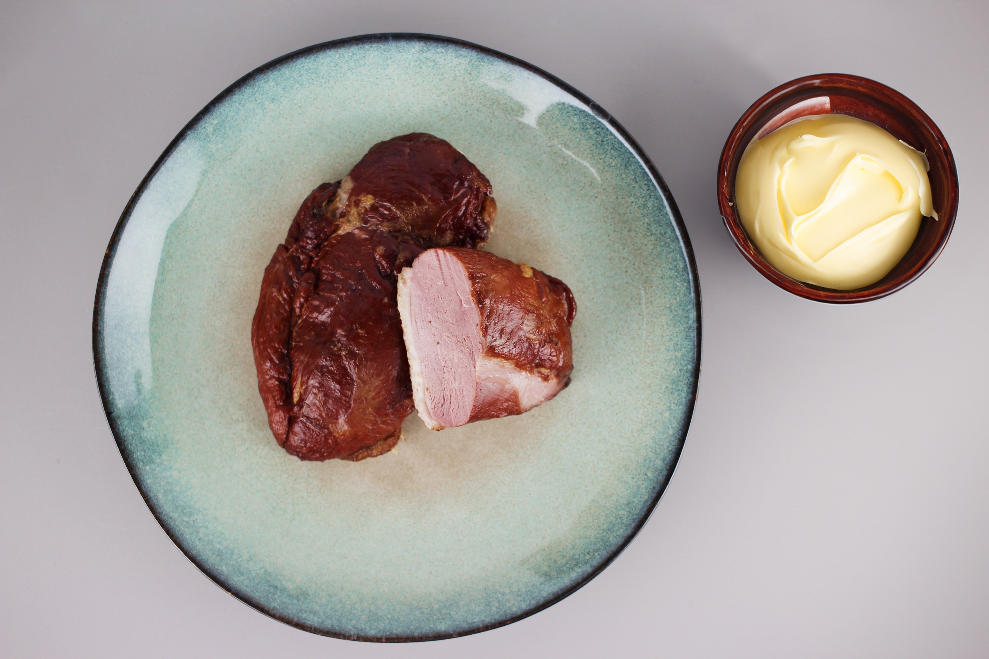 Geräucherte Entenbrust, eine Scheibe geschnitten, auf blau-grünem Teller neben einer Schale mit Butter