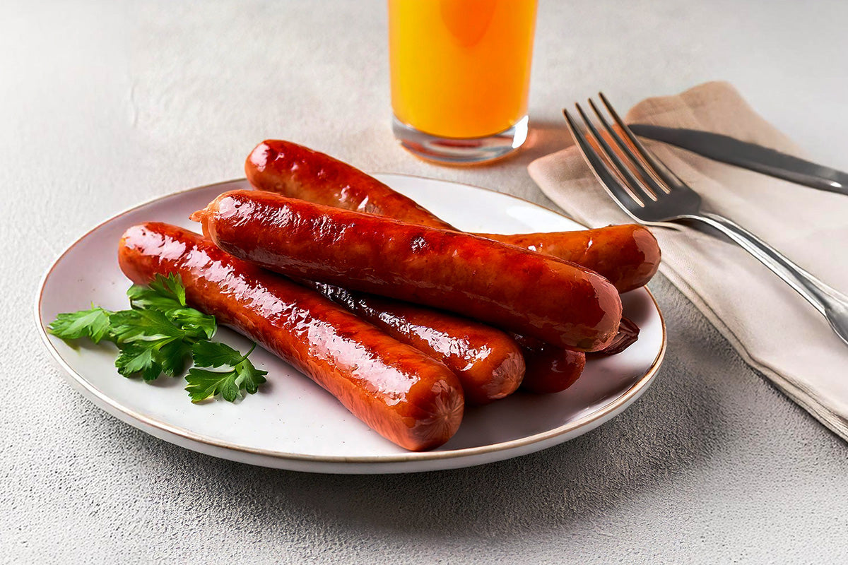 Ein Teller mit 5 gerillten Grillkrakauern, garniert mit frischer Petersilie, dazu ein Glas Orangensaft.