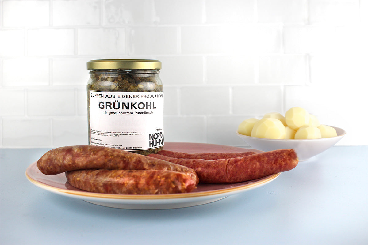 Glas Grünkohl mit geräuchertem Putenfleisch, zwei Pinkel Würste und zwei Kochwürste auf Teller und geschälte Kartoffeln in Schale