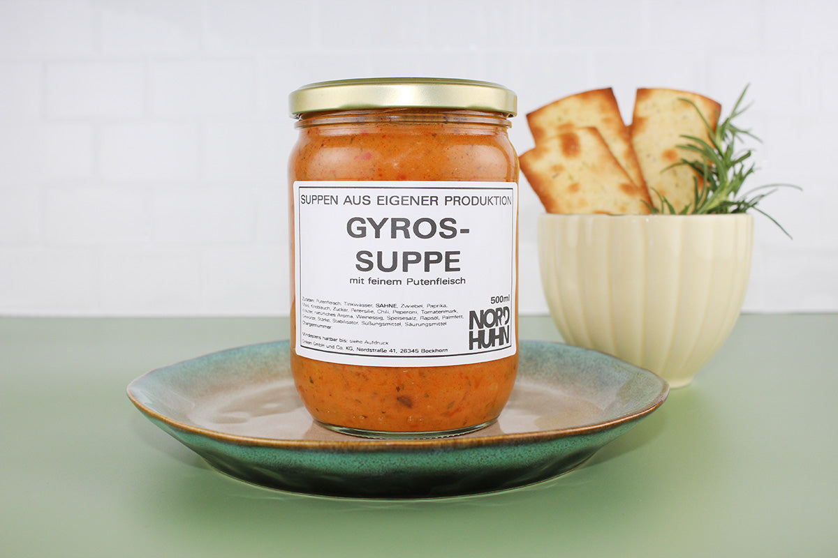 Ein Glas Gyrossuppe mit feinem Putenfleisch von Nordhuhn auf einem Teller, daneben ein Becher mit Brot und Rosmarin