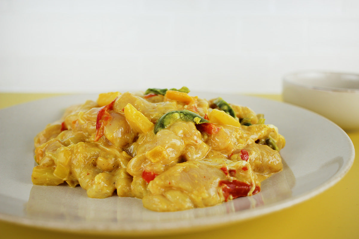 Hähnchenfiletpfanne mit gelber Currysoße, roten Paprikastücken und grünem Gemüse auf weißem Teller