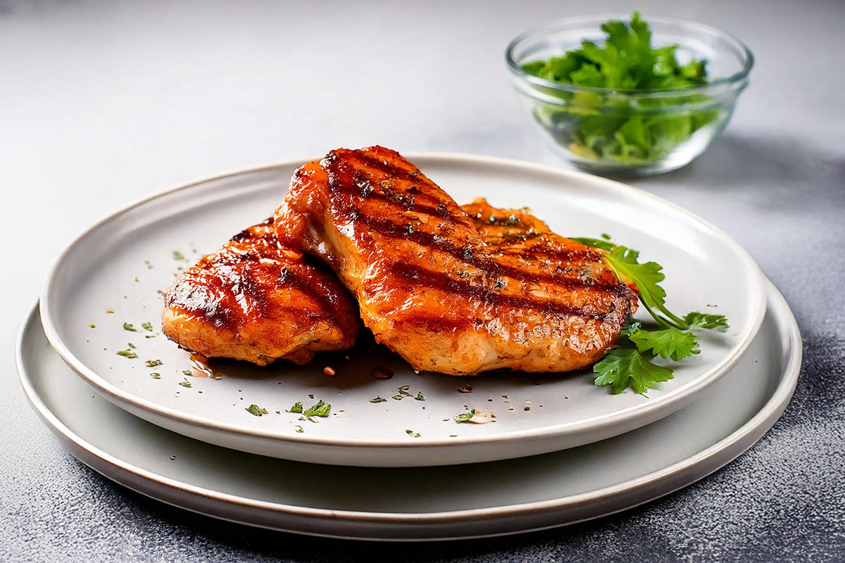 Zwei gegrillte BBQ-Hähnchensteaks mit Grillstreifen auf weißem Teller, garniert mit frischer Petersilie und Kräutern