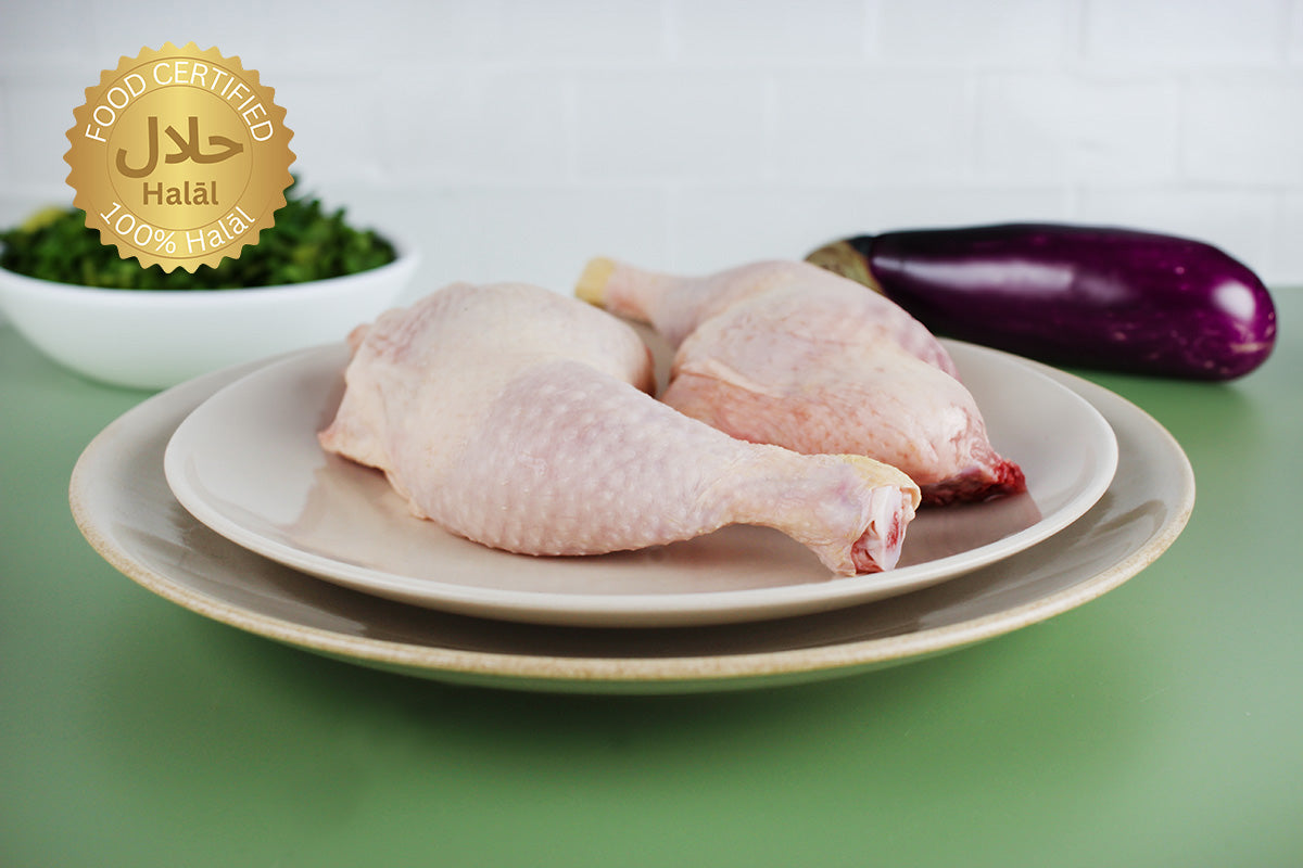 Zwei rohe Hähnchenkeulen auf weißen Tellern, im Hintergrund eine Aubergine und eine Schale mit grünen Kräutern, Halal-Zertifikatssiegel