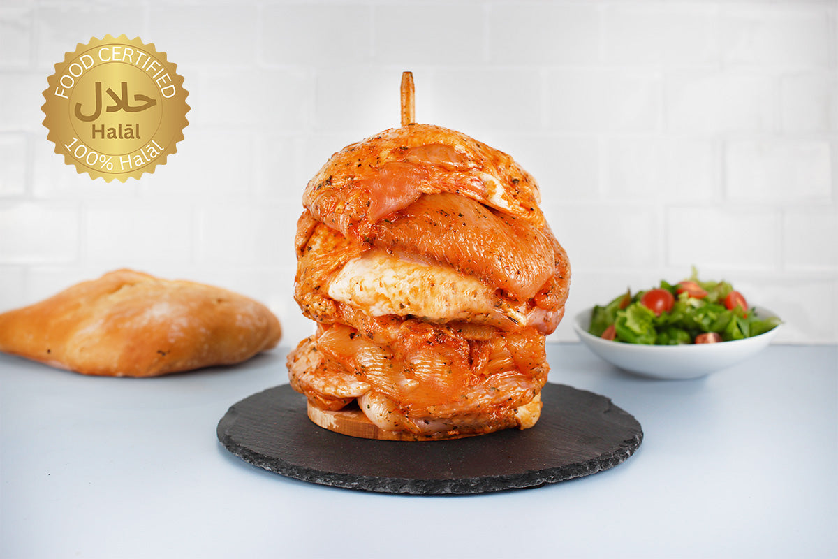 Halal-zertifizierter Hähnchendönerspieß mit mariniertem Fleisch auf schwarzem Stein, Brot und Salat im Hintergrund