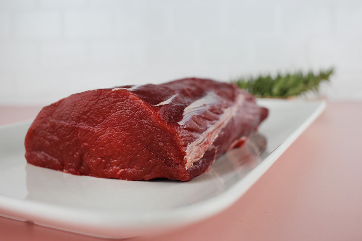 Roher Hirschrücken auf weißem Teller mit Rosmarinzweig im Hintergrund