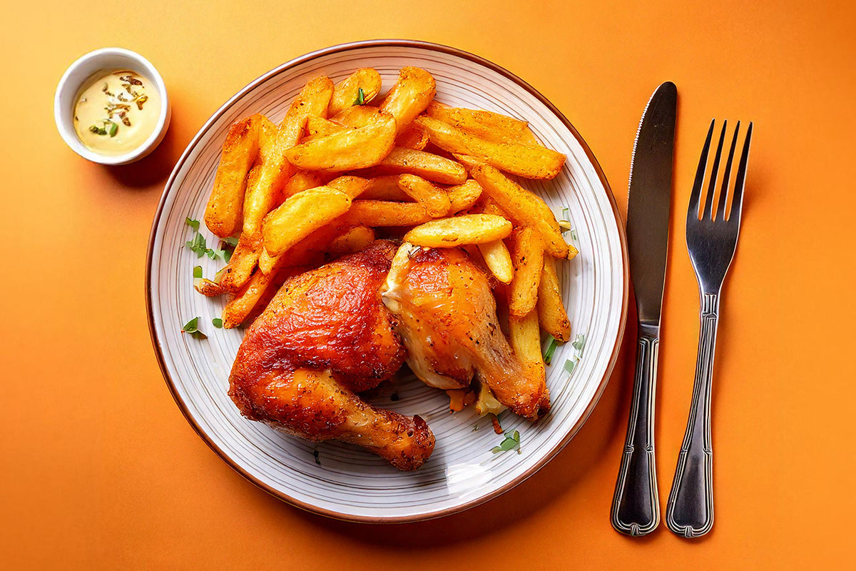 Teller mit zwei gebratenen Hähnchenschenkeln und selbstgemachten Pommes, daneben Messer und Gabel, kleine Schale mit Dip