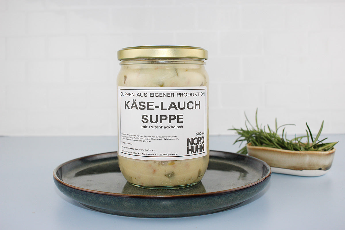 Glas mit Käse-Lauch-Suppe mit Putenhackfleisch von Nordhuhn, 500 ml, auf dunklem Teller, daneben Schale mit frischem Rosmarin