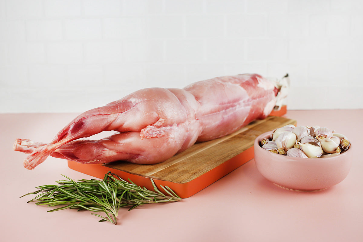 Ausgenommenes Kaninchen auf Holzbrett mit frischem Rosmarin und Schüssel mit Knoblauchzehen