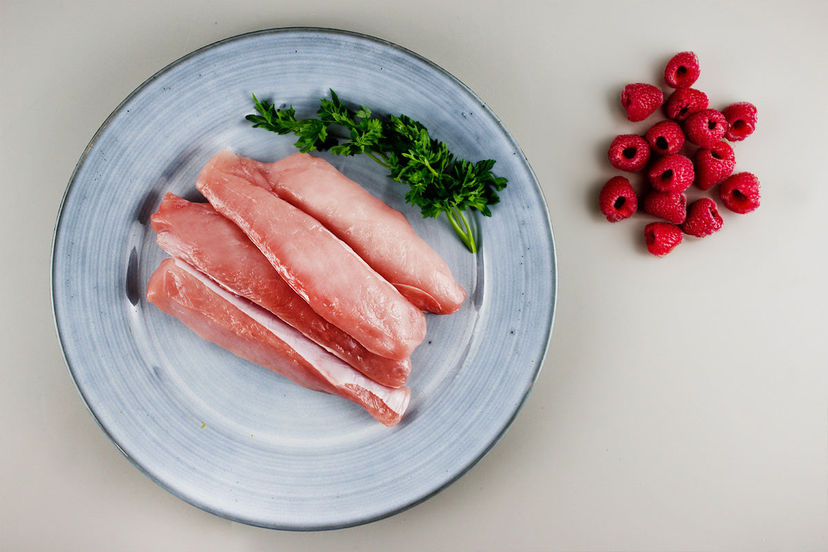 Drei rohe Kaninchenfilets auf einem hellblauen Teller mit frischem Thymian daneben eine Gruppe Himbeeren auf hellem Untergrund