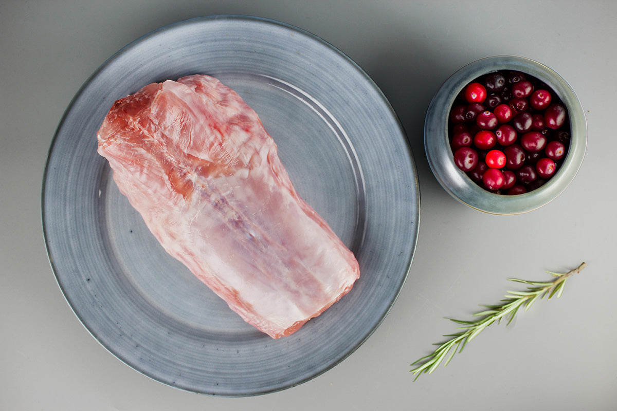 Rohes Kaninchenrückenfleisch auf grauem Teller, daneben Schale mit roten Cranberries und Rosmarinzweig