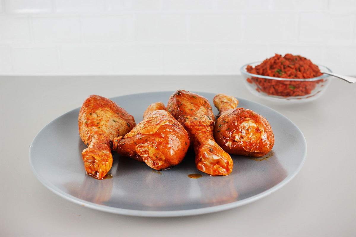 Vier paprikamarinierte Hähnchenschenkel auf einem grauen Teller, im Hintergrund eine Glasschale mit roter Paprikamischung