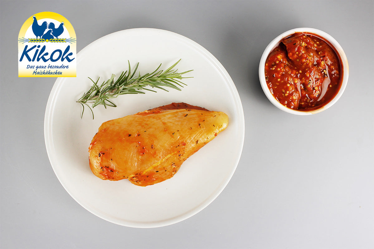 Gegrilltes Hähnchenbrustfilet auf weißem Teller mit Rosmarinzweig, daneben Schale mit BBQ-Sauce, Kikok-Logo oben links