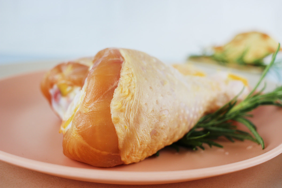 Rohes Kikok-Hähnchenkeulenstück auf einem rosa Teller mit Rosmarinzweig als Garnitur