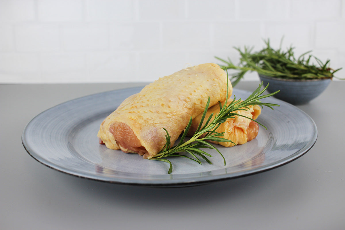 Zwei rohe Kikok-Hähnchensteaks mit Haut auf einem grauen Teller, garniert mit frischem Rosmarin