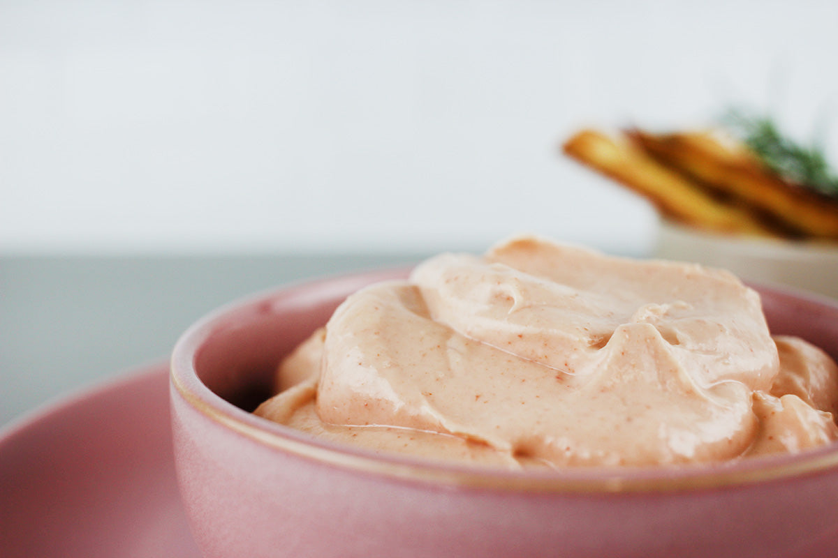 Cremiger, leicht rosa Knoblauchdip in einer rosa Schale, im Hintergrund unscharf Brotsticks