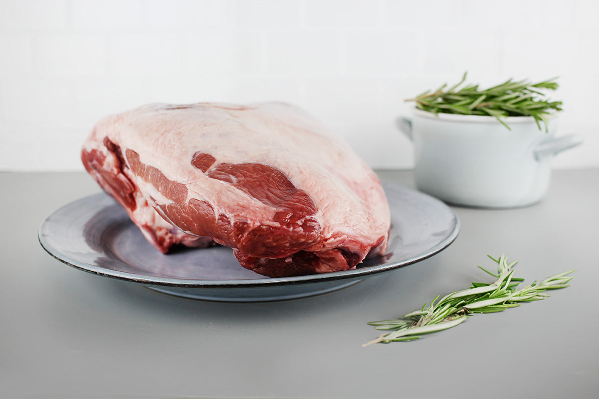 Rohe Lammkeule auf grauem Teller mit frischem Rosmarin auf grauem Untergrund