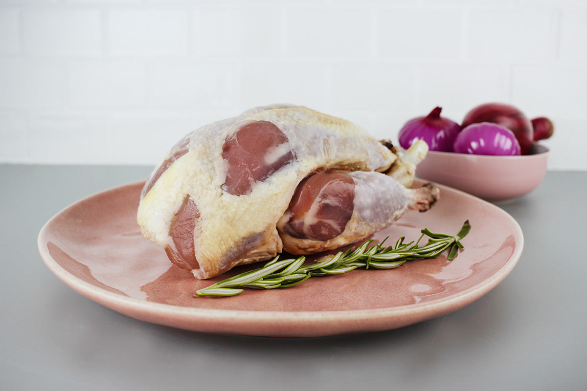 Rohes Perlhuhn auf rosa Teller mit Rosmarinzweig, im Hintergrund Schüssel mit roten Zwiebeln