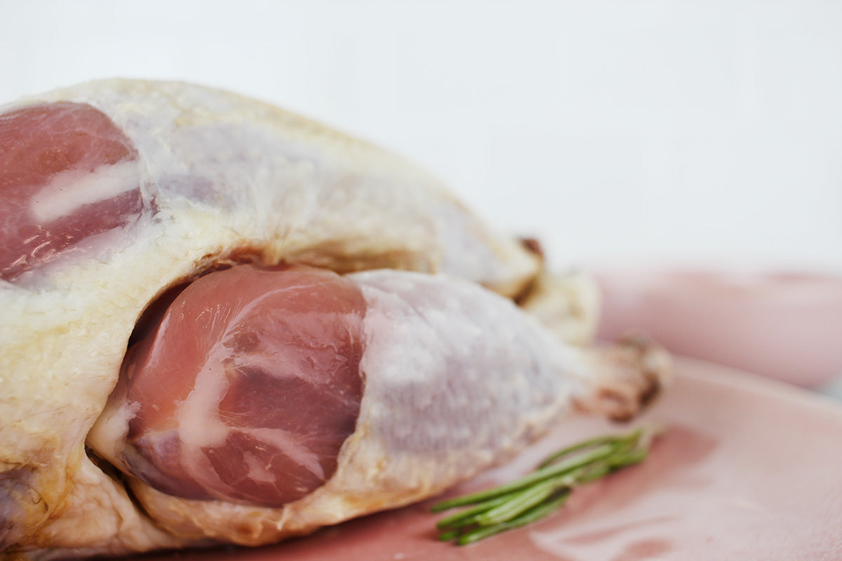 Nahaufnahme von zwei rohen Perlhuhnkeulen mit Haut auf einem Schneidebrett mit einem Zweig Rosmarin