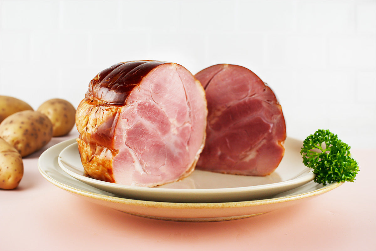 Zwei dicke Scheiben Putenbackschinken auf einem weißen Teller mit Petersilienzweig und Kartoffeln im Hintergrund