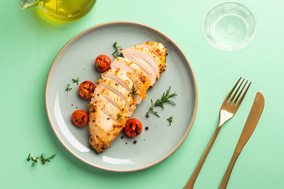 In Scheiben geschnittenes, gebratenes Putenfilet auf grauem Teller mit gegrillten Kirschtomaten und Rosmarin