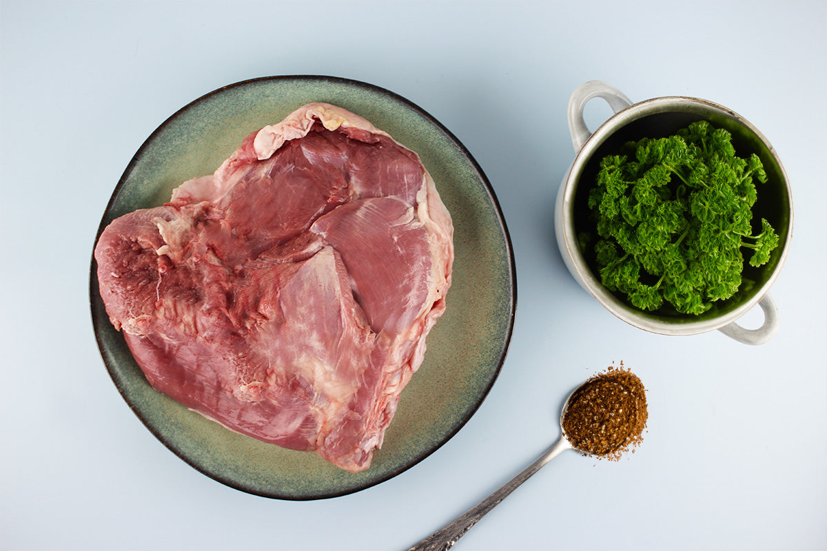 Rohes Putenoberkeulenfleisch auf einem Teller, daneben frische Petersilie in einem Becher und Gewürze auf einem Löffel