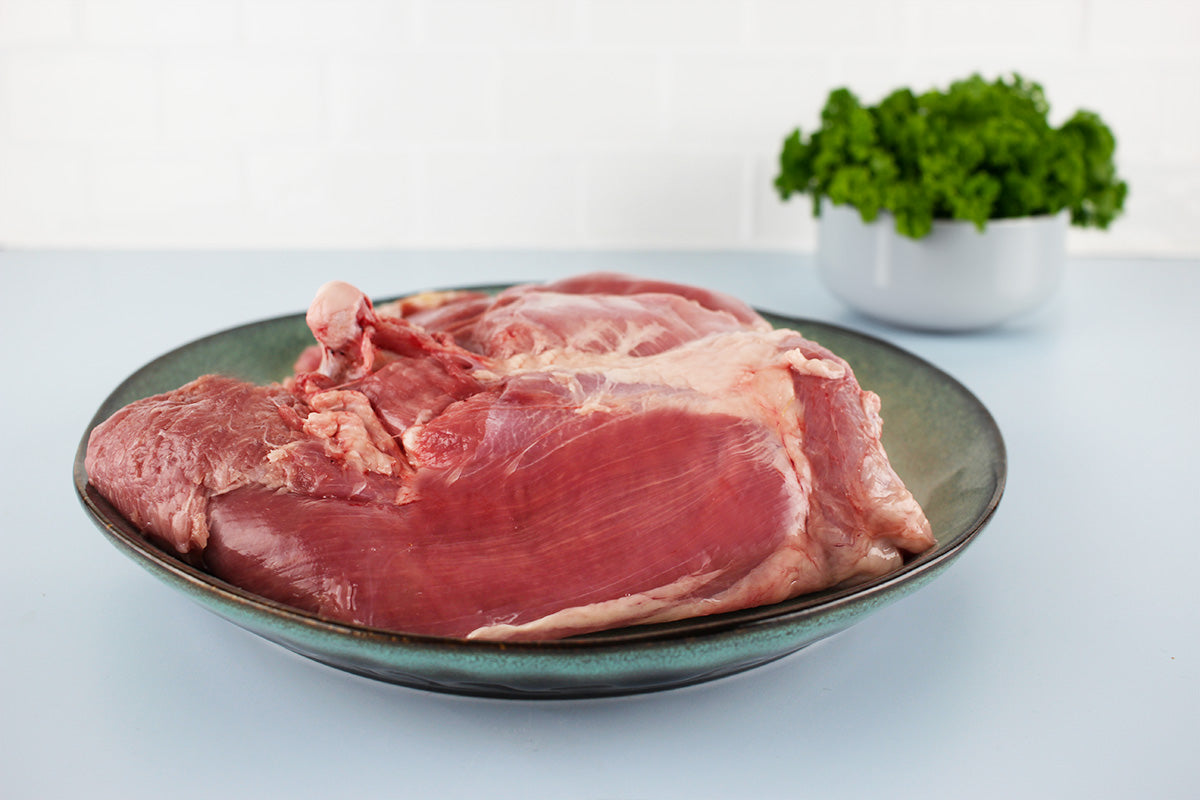 Rohe Putenoberkeule auf einem grauen Teller, im Hintergrund ein Topf mit grünem Salat