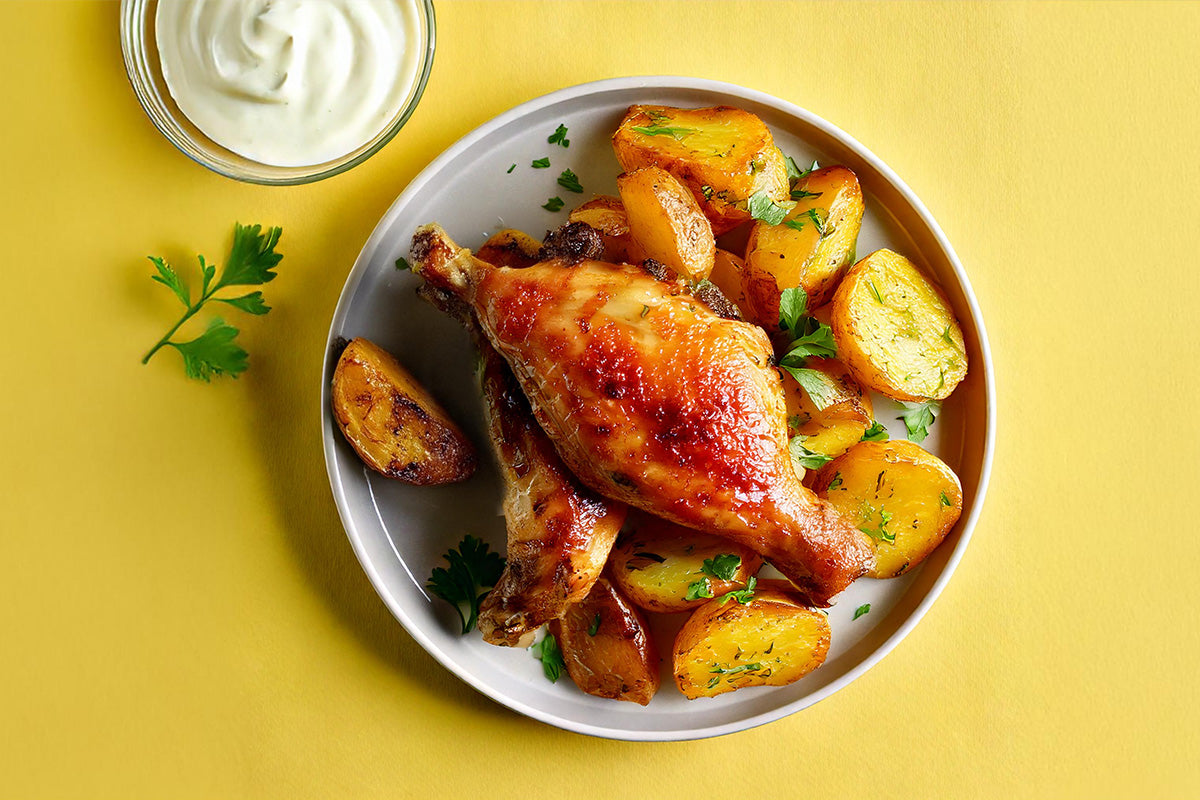 Gebratene Kaninchenkeulen mit goldbraunen Bratkartoffeln und frischer Petersilie auf weißem Teller, daneben Schale mit weißer Sauce