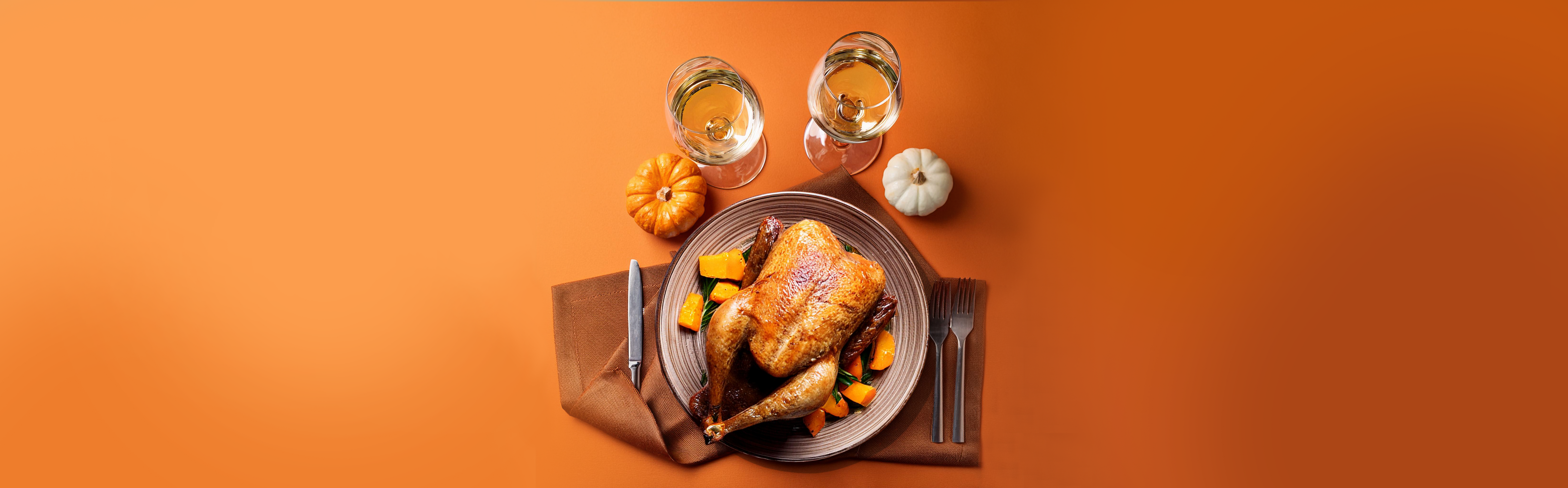 Gebratene Gans auf Teller mit Kürbisstücken, zwei Gläser Weißwein, zwei kleine Kürbisse auf orangefarbenem Hintergrund