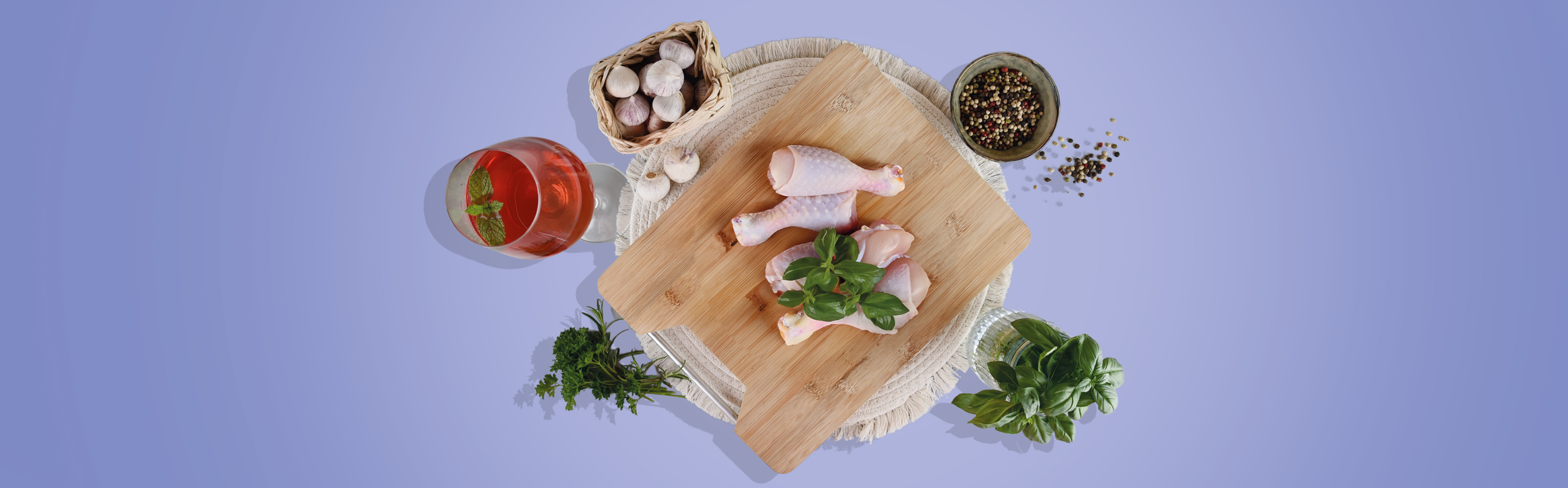 Rohe Hähnchenschenkel auf einem Holzbrett, umgeben von Knoblauch, Pfefferkörnern, frischen Kräutern und einem Glas mit rotem Getränk