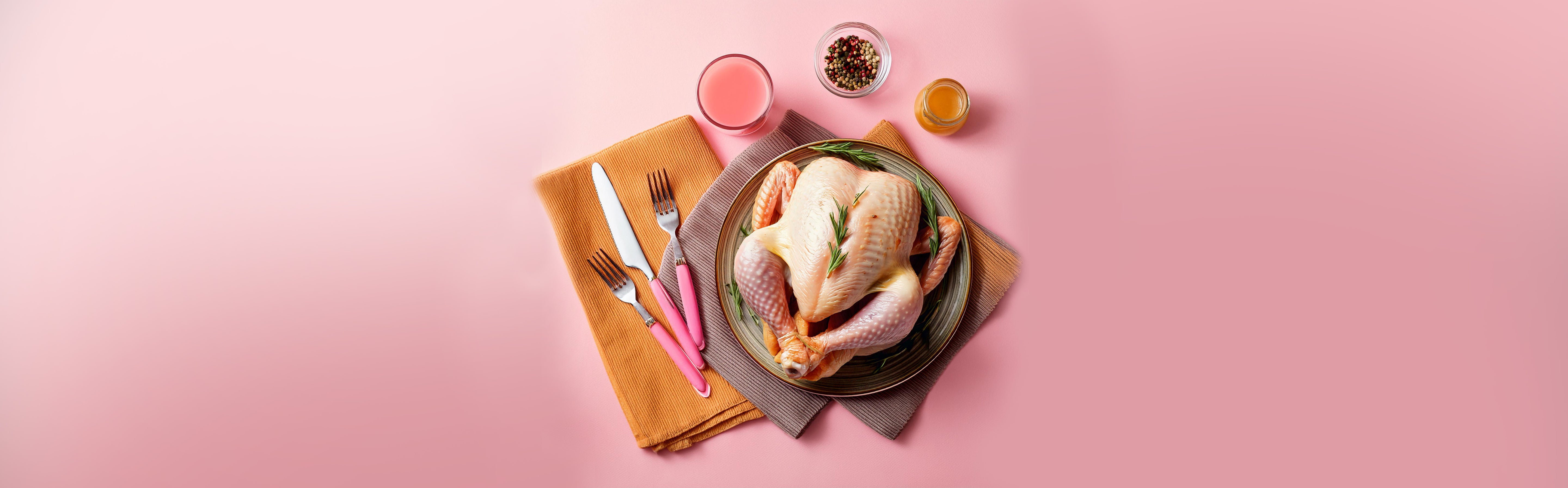 Rohe Pute auf Glasplatte mit Rosmarinzweig, daneben Messer, Gabeln, Pfeffer und zwei Gläser mit Flüssigkeiten auf rosa Hintergrund