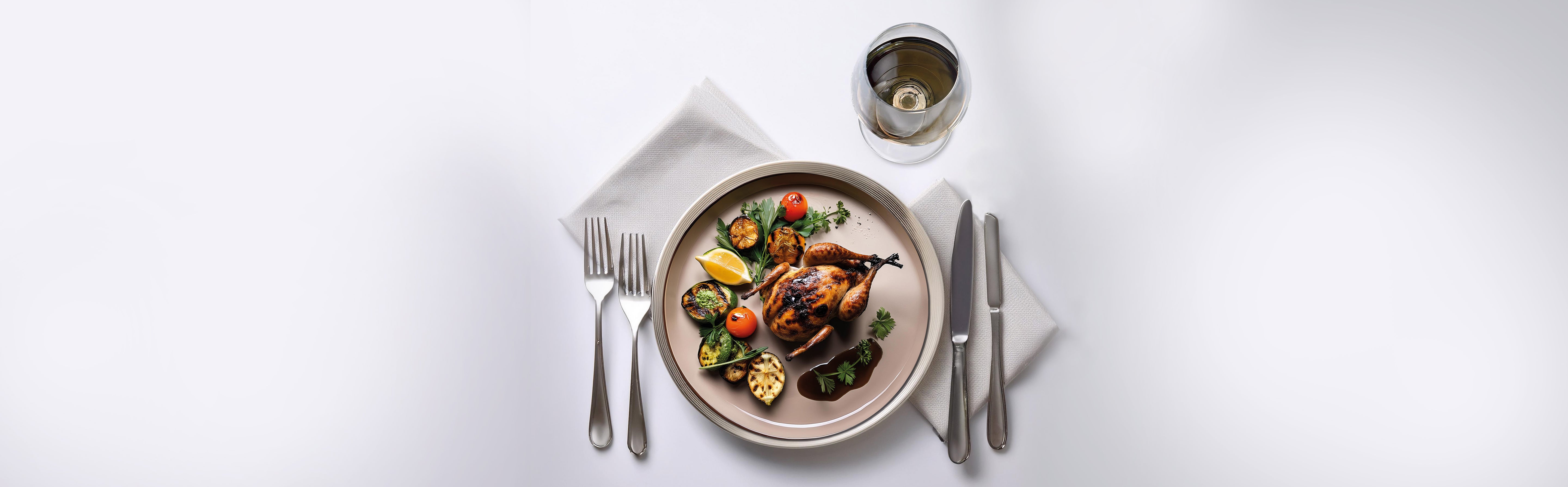 Gebratenes Wachtelgericht mit gegrilltem Gemüse und Sauce auf einem Teller, daneben Besteck und ein Glas Weißwein