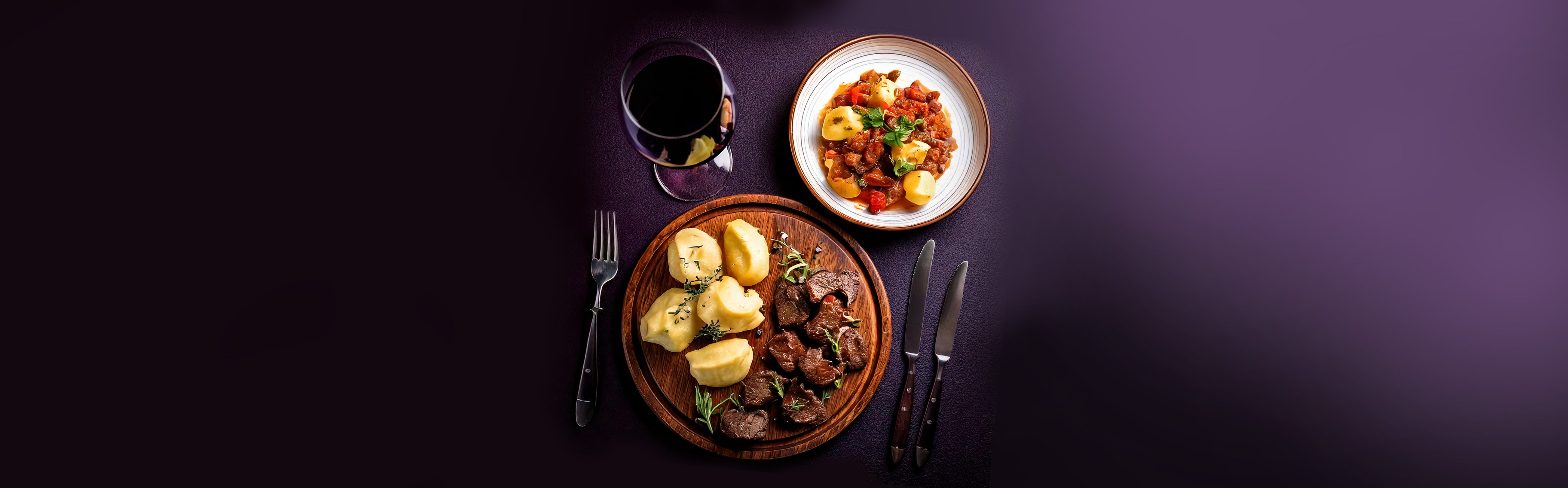 Wildfleisch mit Kartoffeln und Gemüse auf Holzbrett, dazu ein Glas Rotwein und ein Teller mit Gemüse