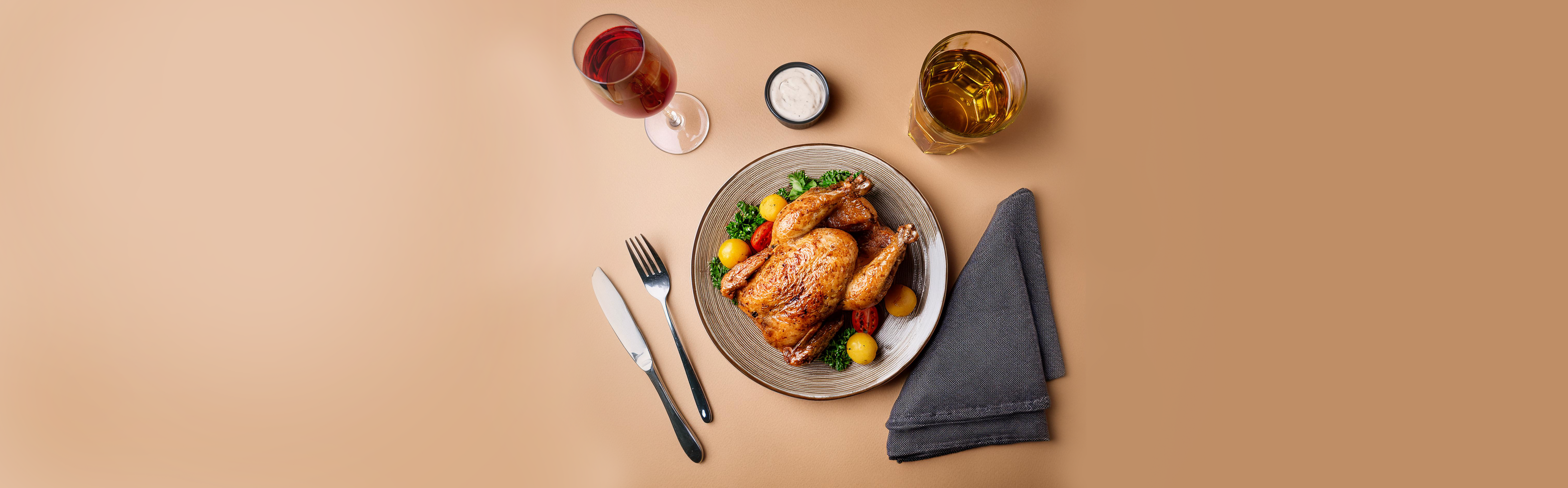 Ganzes gebratenes Perlhuhn auf einem Teller mit Kirschtomaten und Kräutern, daneben Messer, Gabel, Serviette, Glas Rotwein und Glas Saft