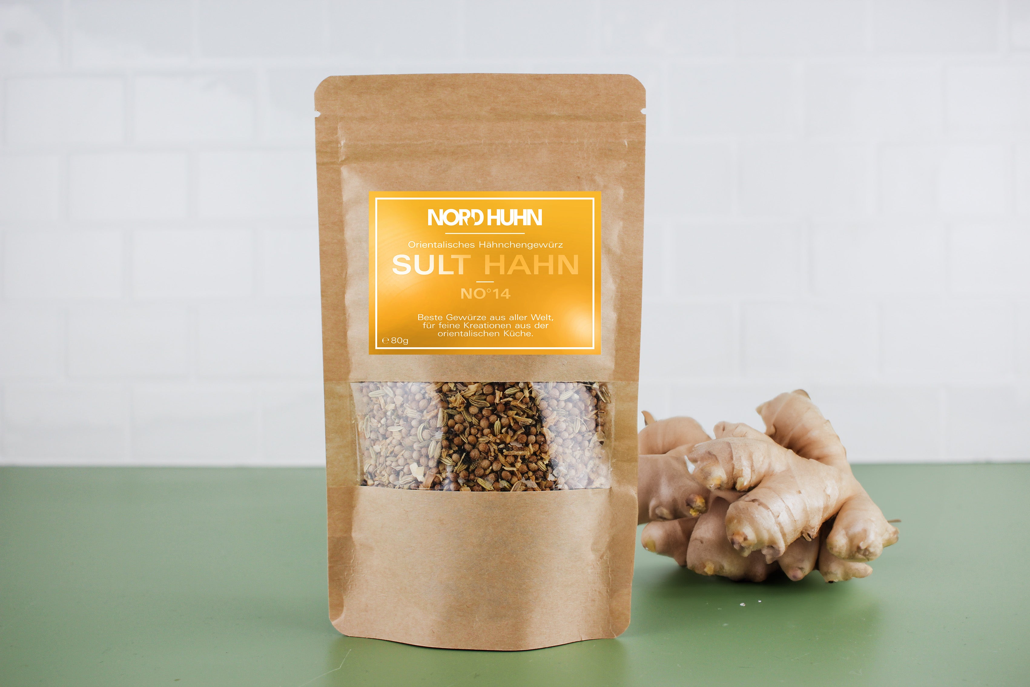 Braune Verpackung mit orientalischem Hähnchengewürz 'Sult Hahn No 14' von Nord Huhn, daneben frische Ingwerwurzel