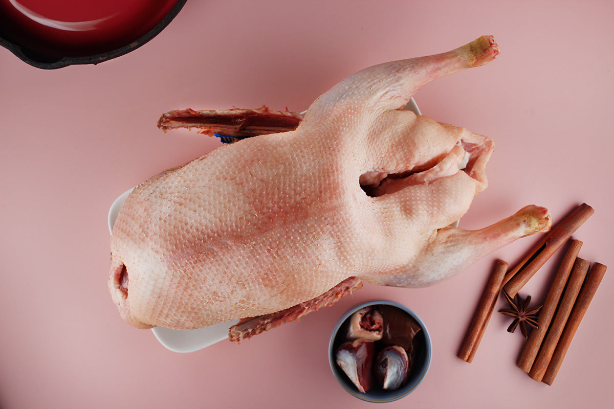 Rohe Gans auf weißem Teller, daneben Zimtstangen und Sternanis auf rosa Untergrund