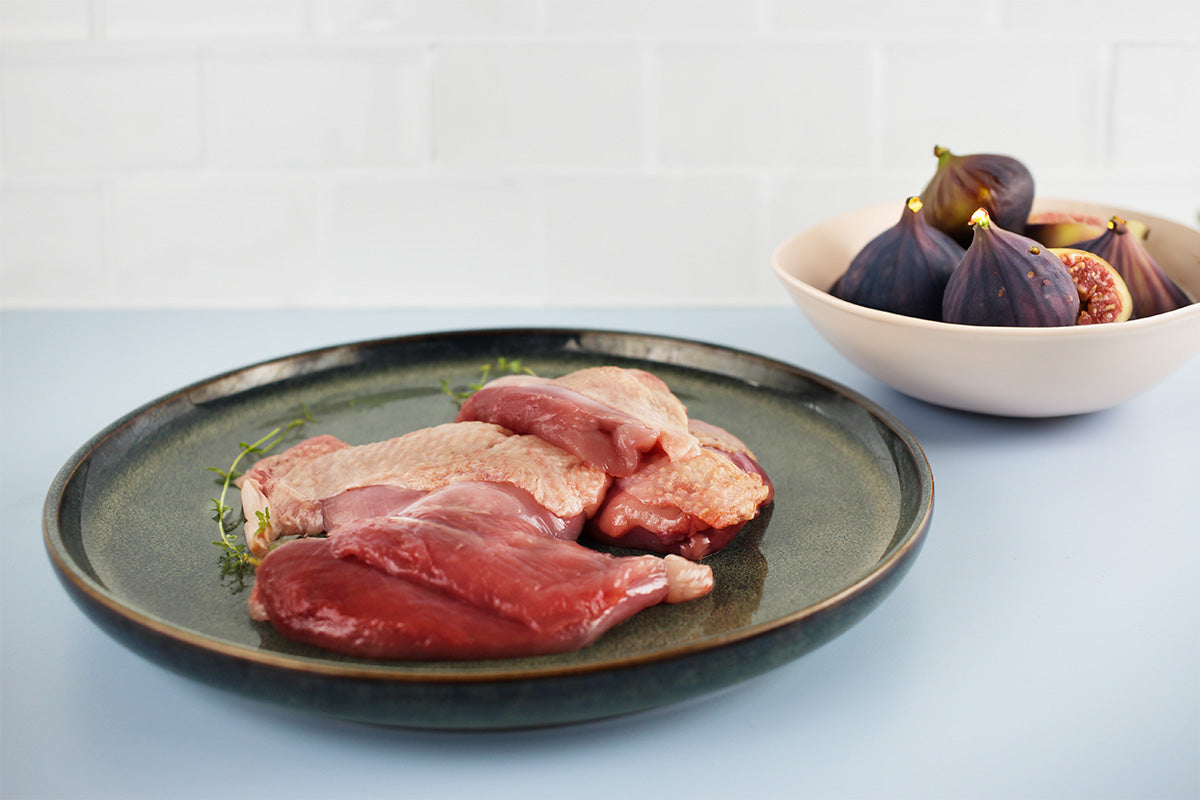 Mehrere rohe Wachtelbrustfilets auf einem dunklen Teller mit frischem Thymian, daneben eine Schale mit frischen Feigen