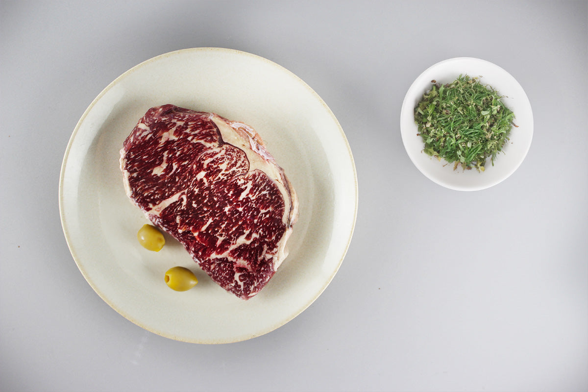 Rohes Wagyu Rumpsteak mit sichtbarer Marmorierung, daneben ein Zweig Rosmarin auf hellem Untergrund