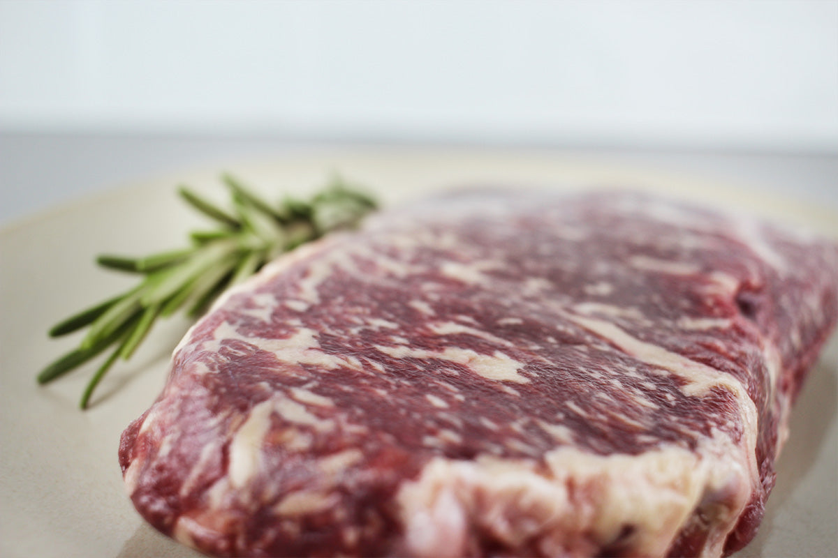 Rohes Wagyu Rumpsteak mit sichtbarer Marmorierung, daneben ein Zweig Rosmarin auf hellem Untergrund