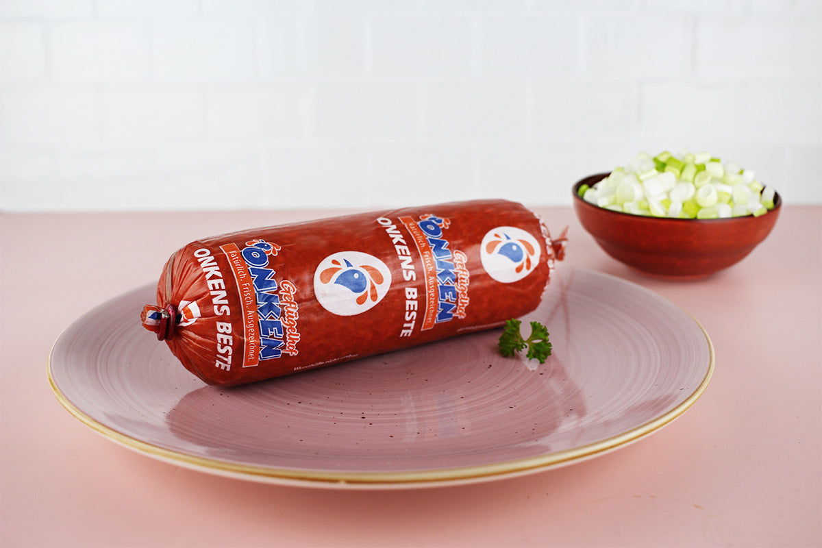 Runde rote Salami mit Aufschrift 'Onkens Beste' auf einem rosa Teller, daneben eine Schale mit geschnittenen Frühlingszwiebeln