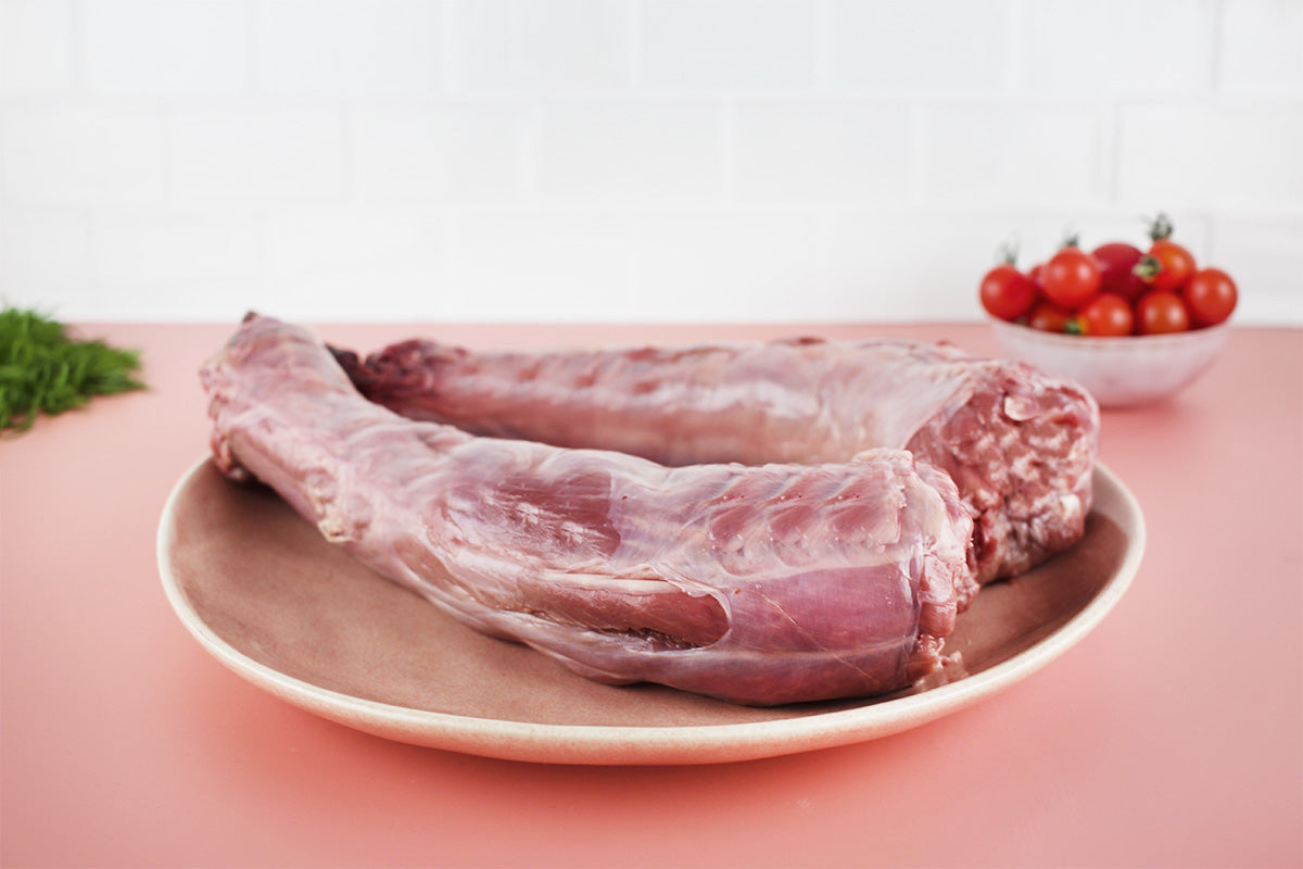 Zwei rohe Putenhälse auf einem braunen Teller, im Hintergrund eine Schale mit Kirschtomaten und etwas Dill