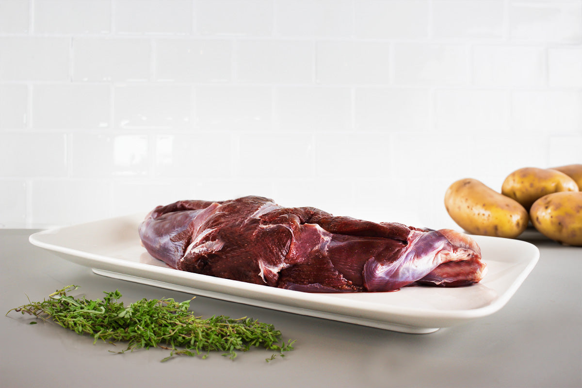 Rohe Wildhasenkeule auf weißem Teller, daneben frischer Thymian und mehrere Kartoffeln auf grauer Arbeitsfläche.