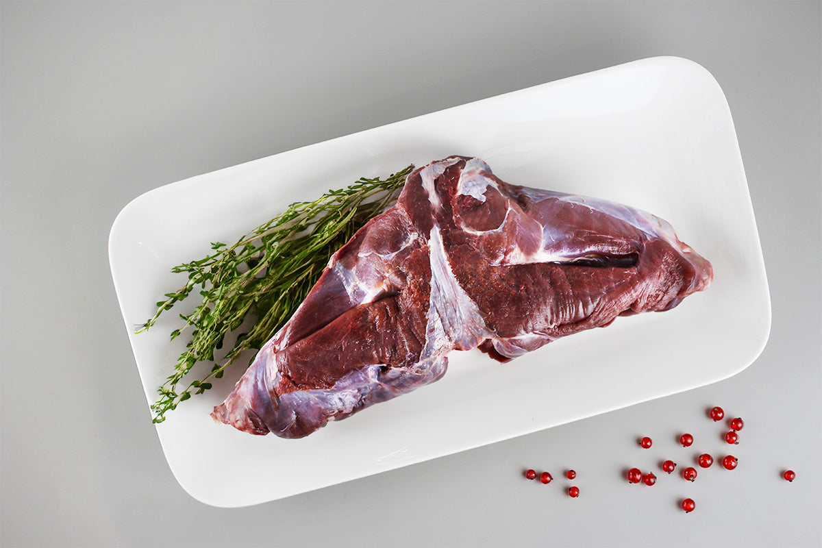 Rohe Wildhasenkeule auf weißem Teller mit frischem Thymian und roten Pfefferkörnern auf grauem Untergrund.